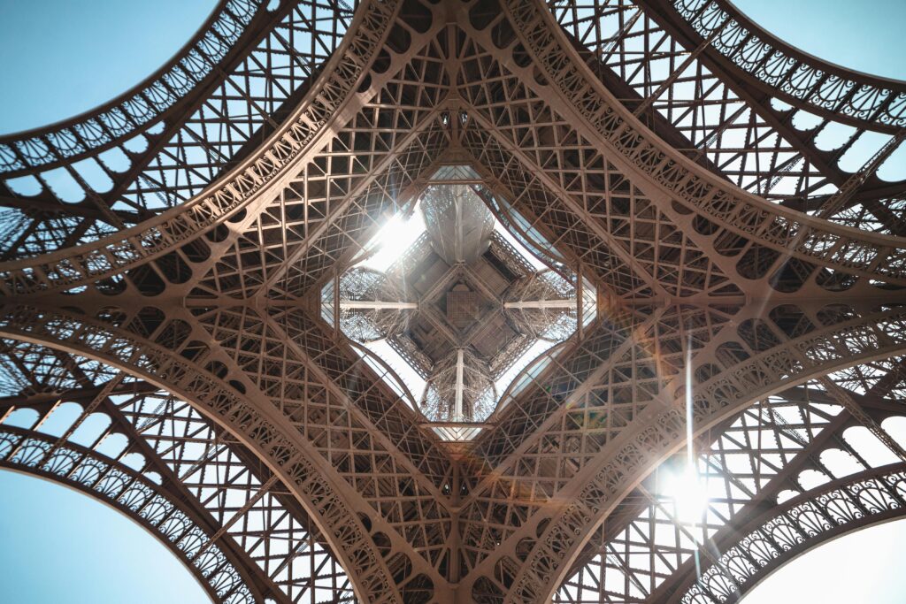 A unique low-angle view of the Eiffel Tower's intricate steel structure with sunlight streaming through.